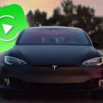 Carro Tesla preto com logotipo de autopiloto e ícone de reprodução, simbolizando uso de apps em modo autopilotado, numa estrada ao pôr do sol.
