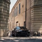 Carro elétrico Polestar 2 Long Range Dual Motor Performance estacionado numa rua estreita de cidade europeia, com edifícios históricos ao fundo, destacando-se pelo design moderno e sustentável.